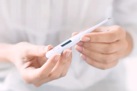 Hände halten ein digitales Thermometer, das die Temperatur für den Eisprung anzeigt.