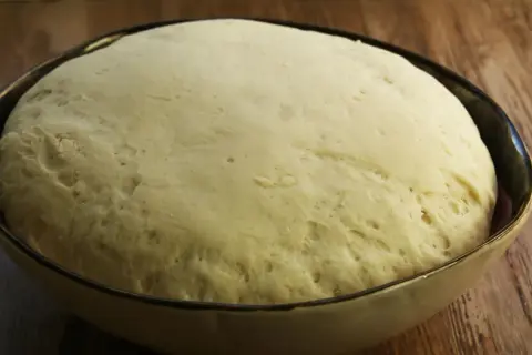 Puszyste ciasto na pizzę wyrosło w misce, gotowe do dalszej obróbki.