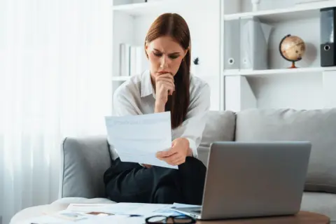 Zamyślona kobieta analizuje dokumenty, zastanawiając się, czy odpowiedź na pozew doręcza się pełnomocnikowi.