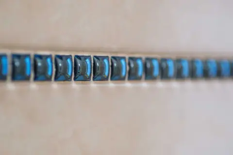 Ligne de petites mosaïques bleues, comme une frise, à une certaine hauteur sur un mur de salle de bain.