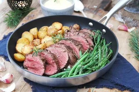 Skivad oxfilé med perfekt innertemperatur, serverad med rostade potatisar och gröna bönor i en stekpanna.