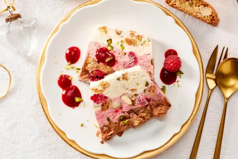 Gefrorener Kuchen mit Beeren, Nüssen und Schokolade auf einem Teller mit Sauce und Löffel.