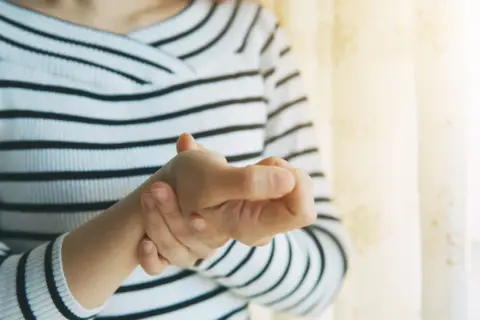 Frau hält ihren Daumen, der schmerzt, als ob sie einen Schnappfinger Daumen hätte.