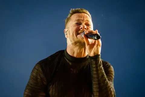 Wokalista Imagine Dragons śpiewa do mikrofonu na tle błękitnego nieba.