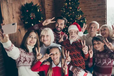 Wesoła rodzina robi sobie świąteczne stylizacje rodzinne selfie przy choince. Wszyscy pozdrawiają gestem pokoju.