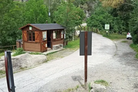 Caseta de información y señalización para senderismo en Aigüestortes. Un camino de grava y asfalto se adentra en un bosque frondoso.