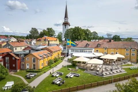 Mariefreds Värdshus med svensk flagga och kyrktorn. Uteservering med parasoller och sittgrupper i gräset.