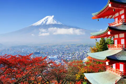 Malownicze widoki Japonii: góra Fudżi w chmurach, miasto i czerwone liście klonu obok czerwonej pagody.