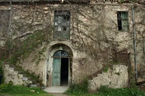 Antica casa in Sardegna, ricoperta di edera, con scale esterne arrugginite e porta verde aperta. Un sogno per chi cerca case a 1 euro.
