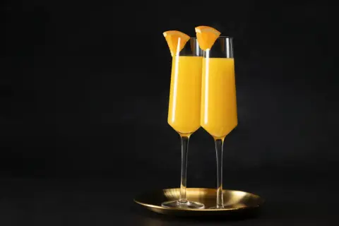 Dwa kieliszki wypełnione złocistym płynem, ozdobione plasterkami pomarańczy. Idealny duet na brunch, klasyczny mimosa.