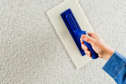 Mano che applica intonaco esterno con frattazzo, creando una texture rustica. Lo spessore intonaco esterno è visibile.