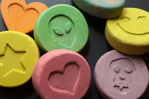 Kolorowe tabletki z symbolami: serce, gwiazda, kosmita, uśmiech, czaszka. To mogą być tabletki MDMA.