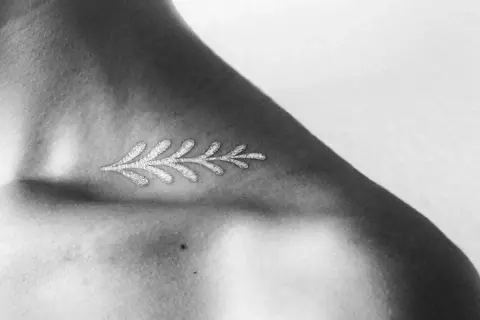 Delicado diseño de rama con **tatuajes blancos en piel negra**, resaltando la delicadeza y el contraste en el hombro.