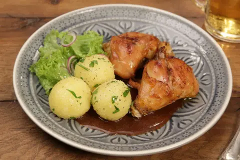 Saftiger Hasenbraten Hausfrauenart mit Klößen, Salat und dunkler Soße auf einem gemusterten Teller.