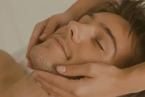Un uomo rilassato riceve un massaggio al viso. Scopri il nostro corso di massaggio gratuito per imparare tecniche di benessere.