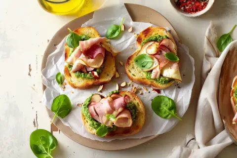 Aromatyczne kanapki z pesto, szynką i świeżą bazylią, posypane migdałami. Idealne na szybką przekąskę.