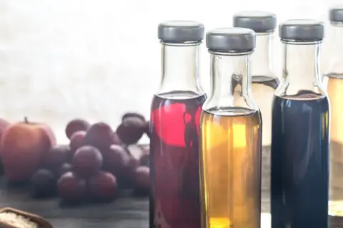 Flaschen mit verschiedenen Essigsorten, Äpfel und Trauben. Essigwasser gesund für den Körper.