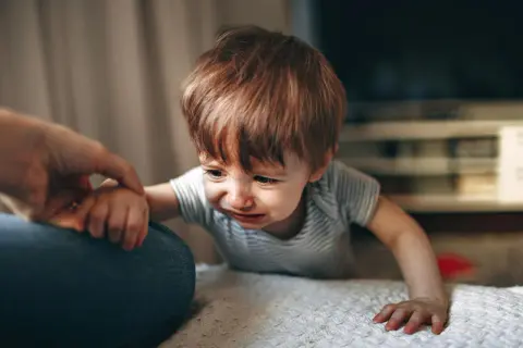 Małe dziecko płacze, gdy mama wychodzi. Trzyma się jej ręki, nie chcąc jej puścić.