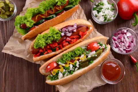 Trzy apetyczne hot dogi z sałatą, pomidorami, ogórkiem, cebulą i papryką. Idealne na letnie grillowanie!