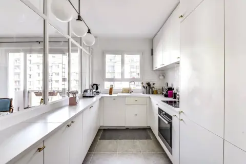 Cuisine en longueur plan, blanche et lumineuse, avec plan de travail en marbre, évier, four et rangements.