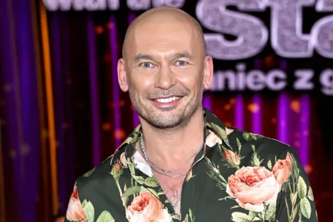 Tomasz z "Tańca z Gwiazdami" w kwiecistej koszuli, uśmiechnięty na tle sceny.