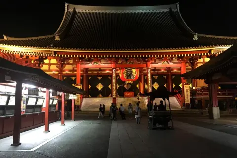 Nocny widok na świątynię Senso-ji z czerwoną latarnią i ludźmi spacerującymi po dziedzińcu.