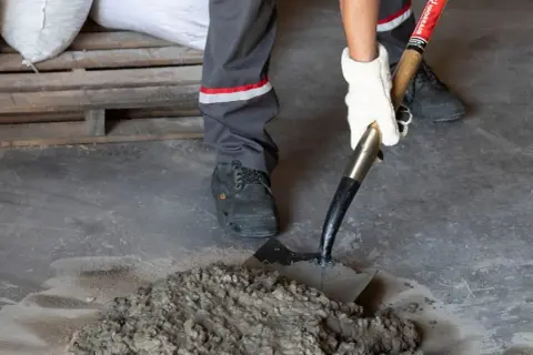 Mano enguantada usa pala para mezclar mortero cemento fresco en el suelo.