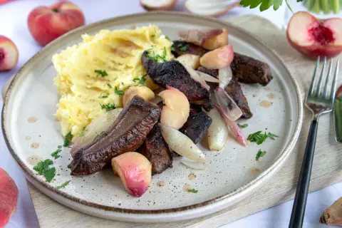 Leber braten ohne Mehl: zarte Leberstücke mit karamellisierten Zwiebeln und Pfirsichspalten, serviert mit cremigem Kartoffelpüree und frischer Petersilie.