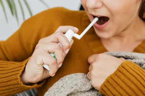 Kobieta aplikuje spray do gardła, łagodząc ból i dyskomfort związany z aftą na migdałku.
