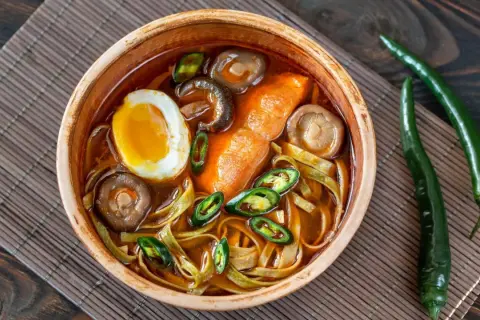 Eine Schüssel Ramen mit Ei, Pilzen und Chili. Der würzige Sud weckt die umami zunge und verspricht ein intensives Geschmackserlebnis.