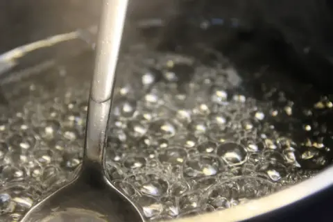 Metalowa łyżka zanurzona w bulgoczącej wodzie, tworzącej bąbelki. To początek pysznej przepalanki.