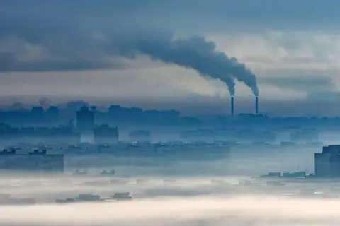 Mglisty poranek nad miastem, z kominów fabrycznych wydobywa się dym. O3 co to za zanieczyszczenie?
