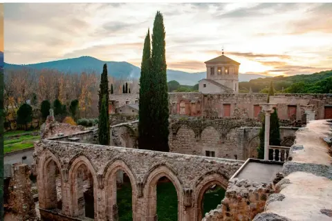 Ruinas de antiguos monasterios cerca de Madrid, con arcos de piedra y cipreses altos bajo un cielo crepuscular.