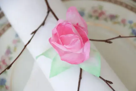 En rosa ros av blommor av kaffefilter, dekorerad med en kvist på en duk.