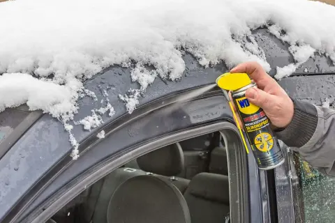 Hand sprüht Silikonspray auf die Gummidichtung des Autos, um sie vor Frost zu schützen und die Gummidichtung zu reparieren.