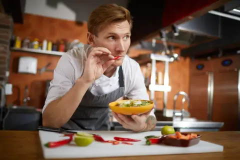 Koch probiert Chili, um scharf essen zu trainieren. Er hält eine Schüssel mit Salat und prüft die Schärfe.