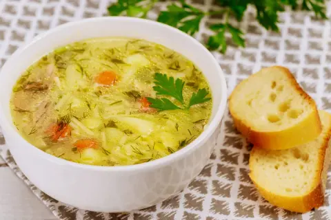 Aromaticzna, tradycyjna zupa jarzynowa z kawałkami mięsa, marchewką i ziemniakami, ozdobiona natką pietruszki. Obok kromki chleba.