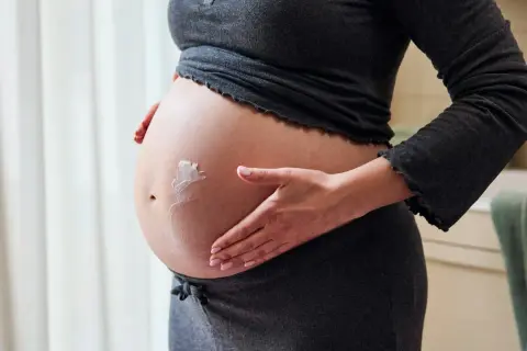 Gravid kvinna smörjer in sin mage med kräm för att motverka torr hud.