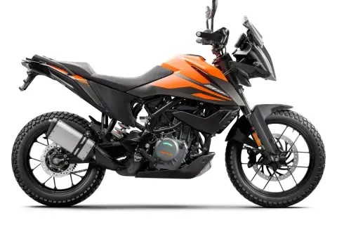 Pomarańczowy motocykl KTM 390 Adventure gotowy na przygodę, z agresywnym designem i terenowymi oponami.