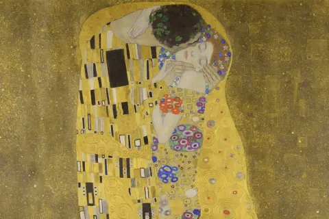 El beso de Gustav Klimt: una pareja abrazada en un campo dorado, ella con flores en el pelo, él con una corona de hojas.