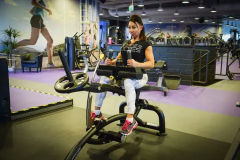 Kvinna tränar magen på gymmaskin. Hon har på sig träningskläder och fokuserar på sin vad press.