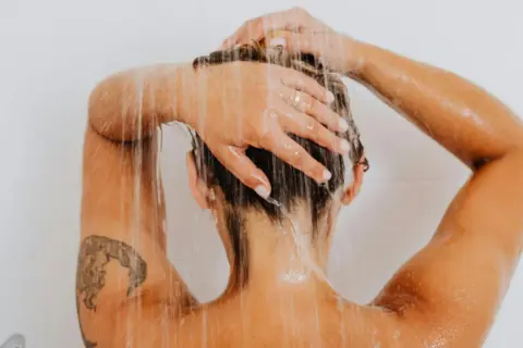 Frauenkopf unter der Dusche, Wasser rinnt über Schultern und Arme mit einem frischen Tattoo.