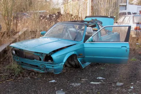 Turkusowy, zniszczony samochód na złomowisku. Drzwi i maska otwarte, jakby ktoś właśnie zaczął zastanawiać się, jak zezłomować auto.
