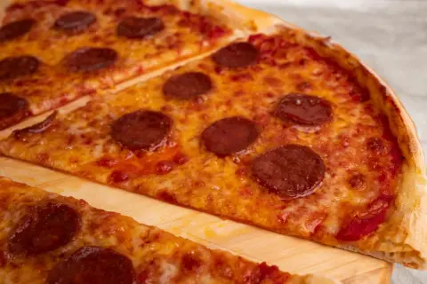 Kawałki pizzy pepperoni z roztopionym serem na desce.