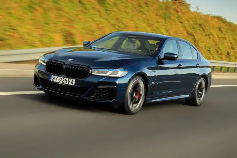 Ciemnoniebieskie BMW 545e pędzi autostradą, otoczone zielenią.