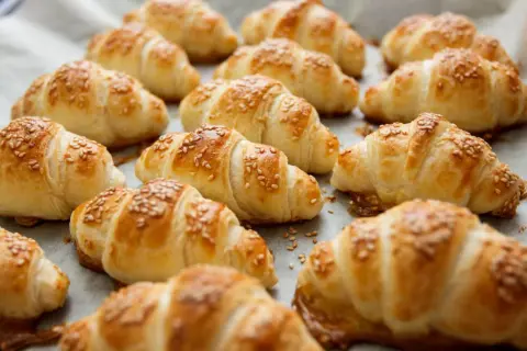 Croissant dorati e fragranti, preparati con pasta sfoglia e cosparsi di semi di sesamo, pronti per essere gustati.