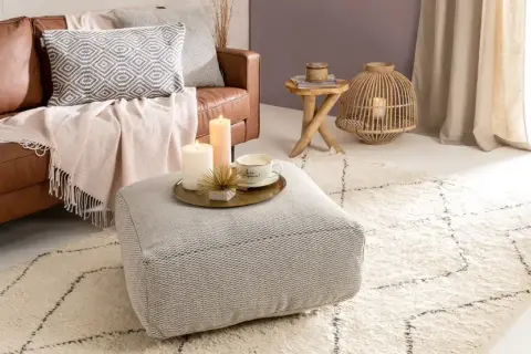 Gemütliches Wohnzimmer im hygge stil mit Ledersofa, Kissen, Decken, Kerzen und einem Teppich.