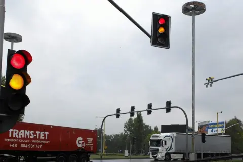 Na skrzyżowaniu widać czerwone i żółte światła. Białe kamery nad światłami monitorują ruch.