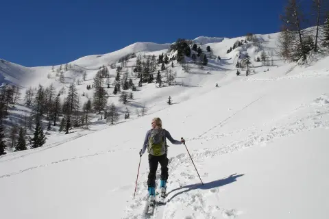 Sciatrice con zaino e bastoncini, in un paesaggio innevato con alberi radi e montagne sullo sfondo. La **forca canapine** è il suo obiettivo.
