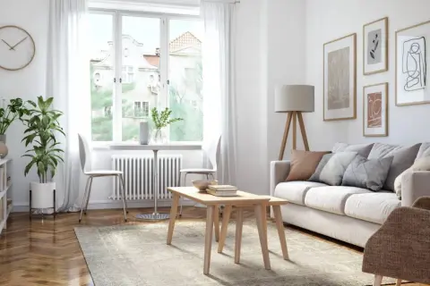 Ein helles Wohnzimmer mit Sofa, Couchtisch, Bücherregal und Pflanzen. Kunstwerke zieren die Wand, während durch das Fenster Tageslicht einfällt.